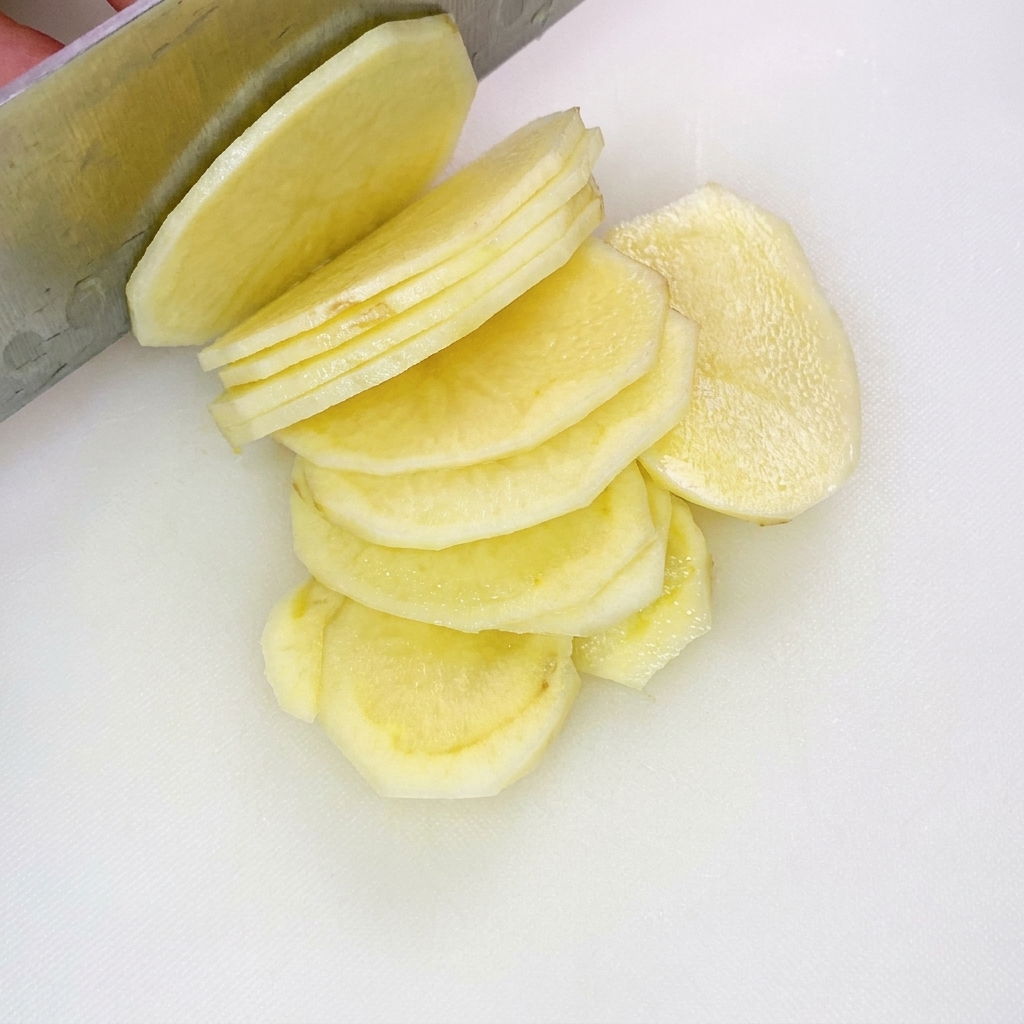 Uniformly cut thin potato strips spread out on a white cutting board.