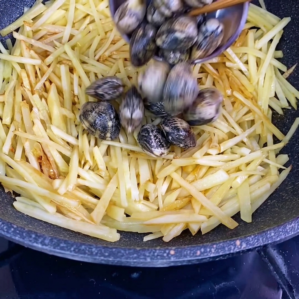 Fresh clams in shells being added to the wok with the seasoned potato strips.