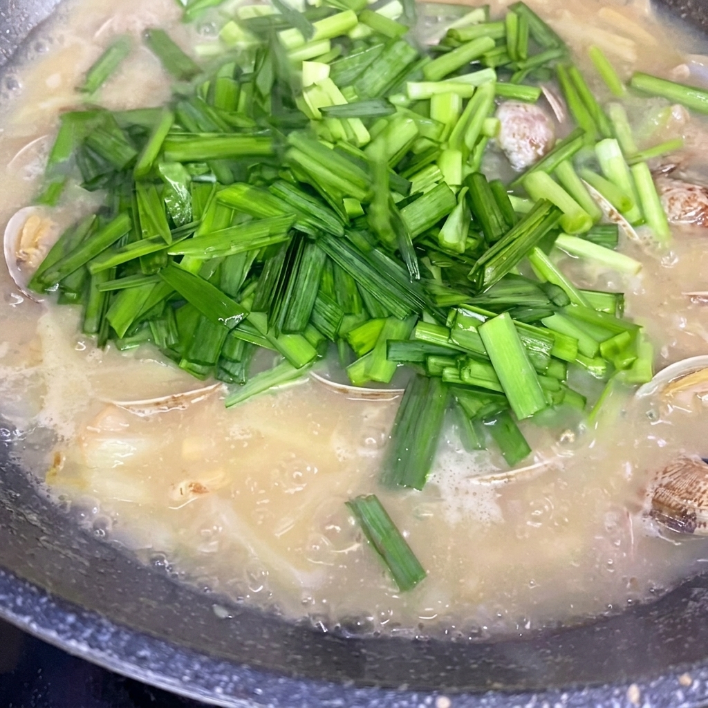 Freshly chopped Chinese chives being sprinkled over a simmering pot of potato and clam soup.