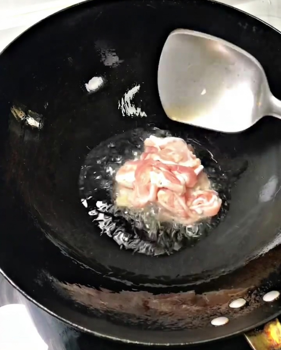 Thin pork slices sizzling in a hot wok with oil, being stirred with a metal spatula.