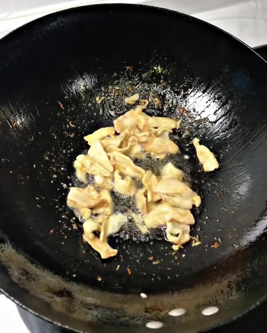 Chopped green onions and ginger being stirred into the pork in a hot wok.