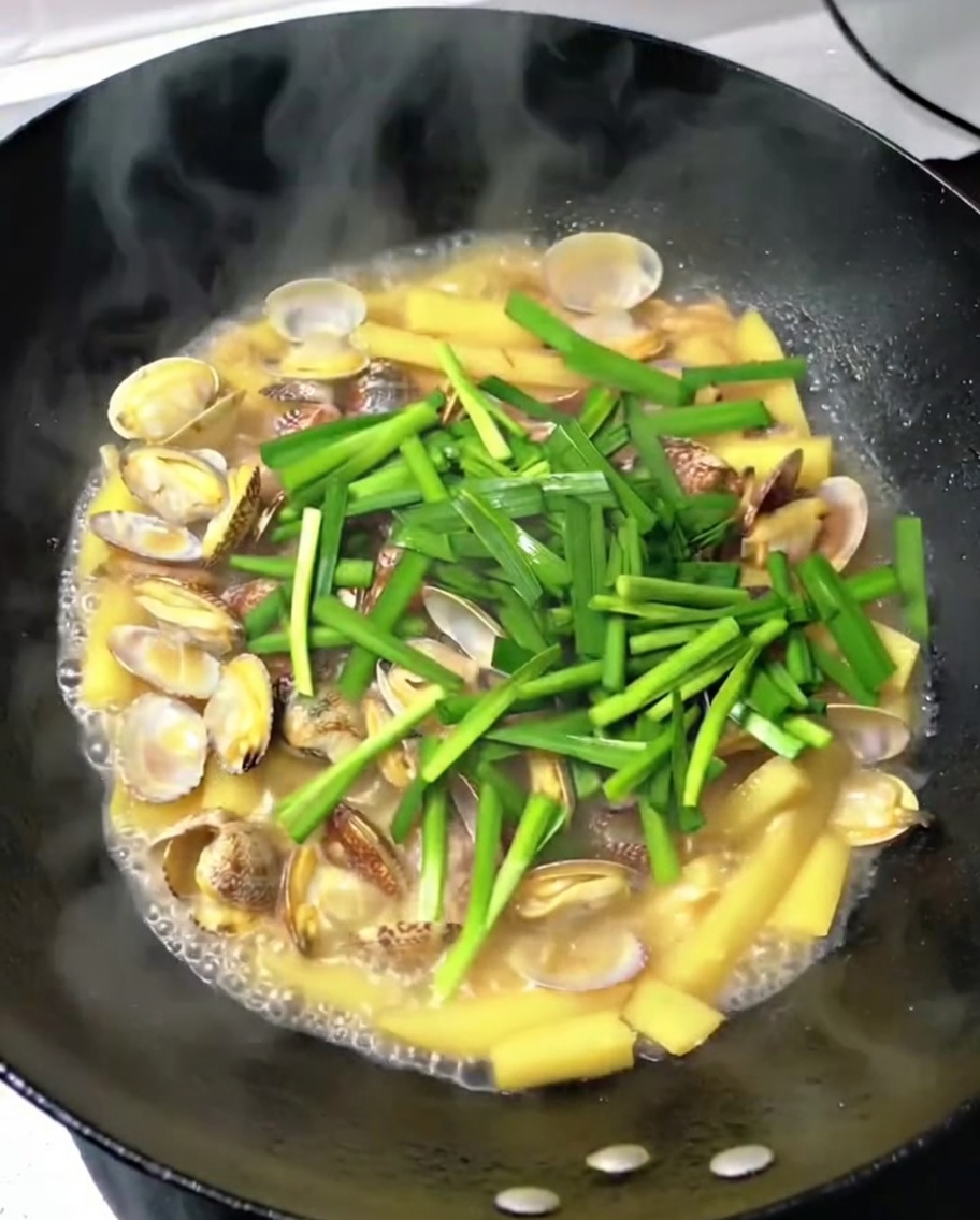 Chopped fresh garlic chives being scattered into the wok with clams, potatoes, and pork.