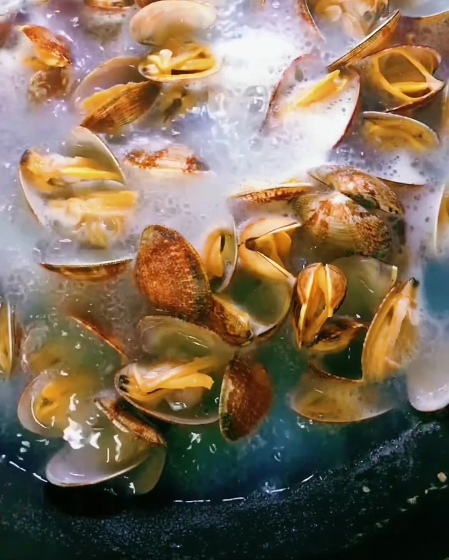 Clams in a pot of boiling water, shells opening up as they cook.