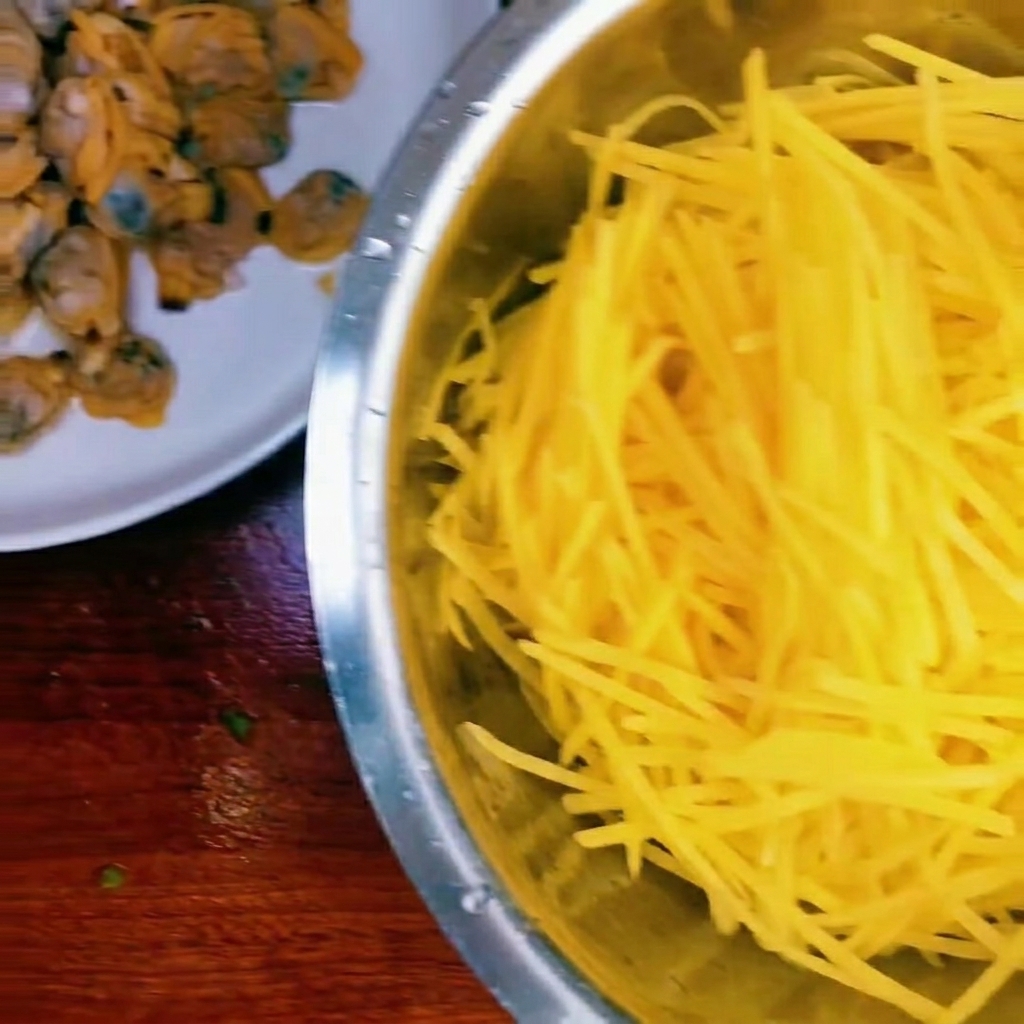 A bowl containing shredded raw potatoes, cooked clam meat, and a small pile of chopped green onions.