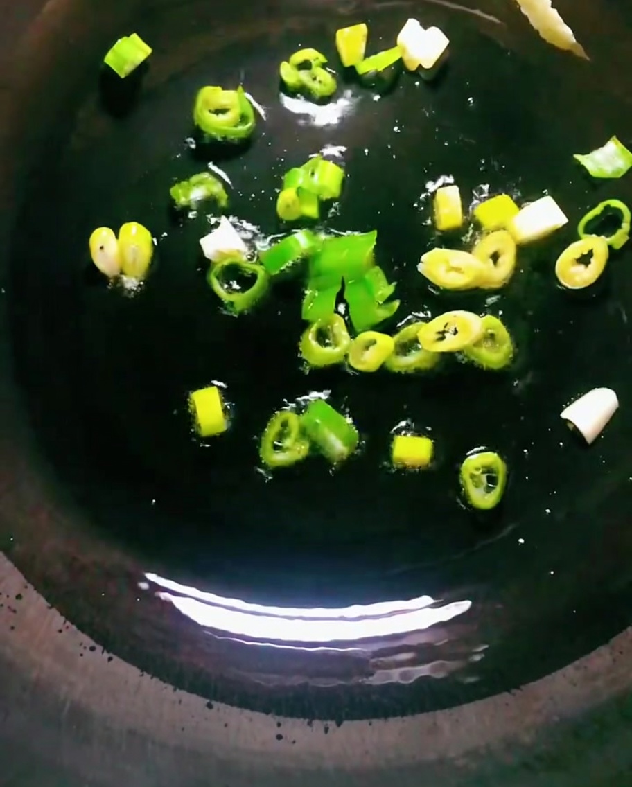 Green onions frying in hot oil in a dark wok.