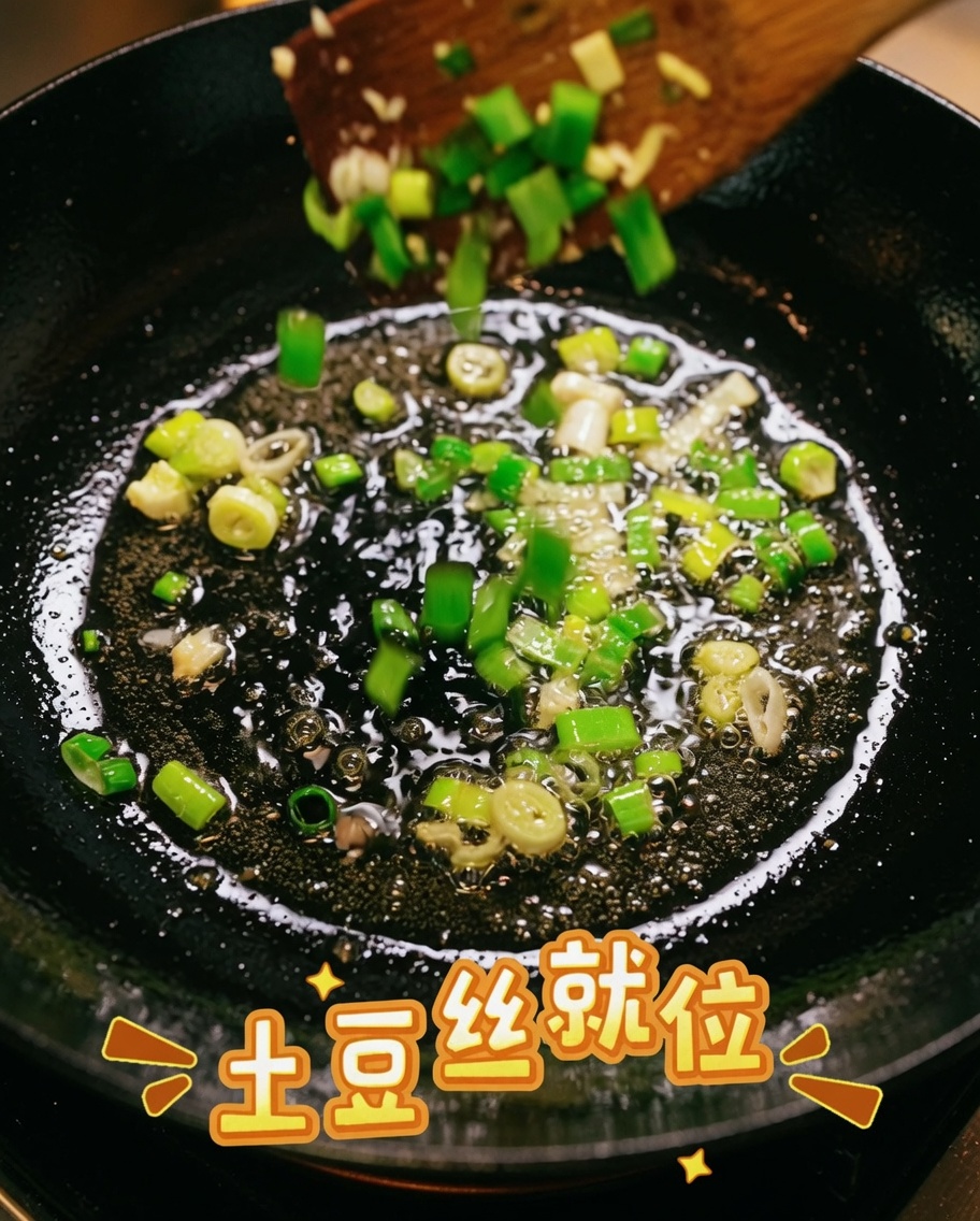 Shredded potatoes being mixed with sautéed green onions in a pan.
