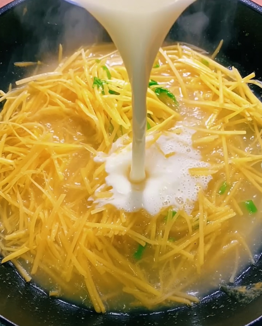Clear liquid being poured from a bowl into a wok containing sautéed potatoes.