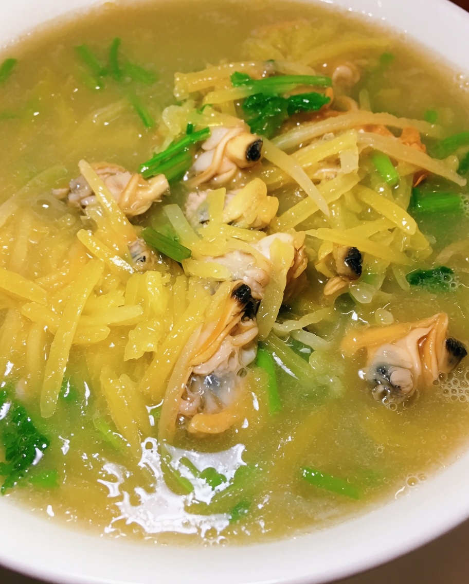 A close-up view of fresh chopped cilantro being sprinkled into a bubbling pot of potato and clam soup.