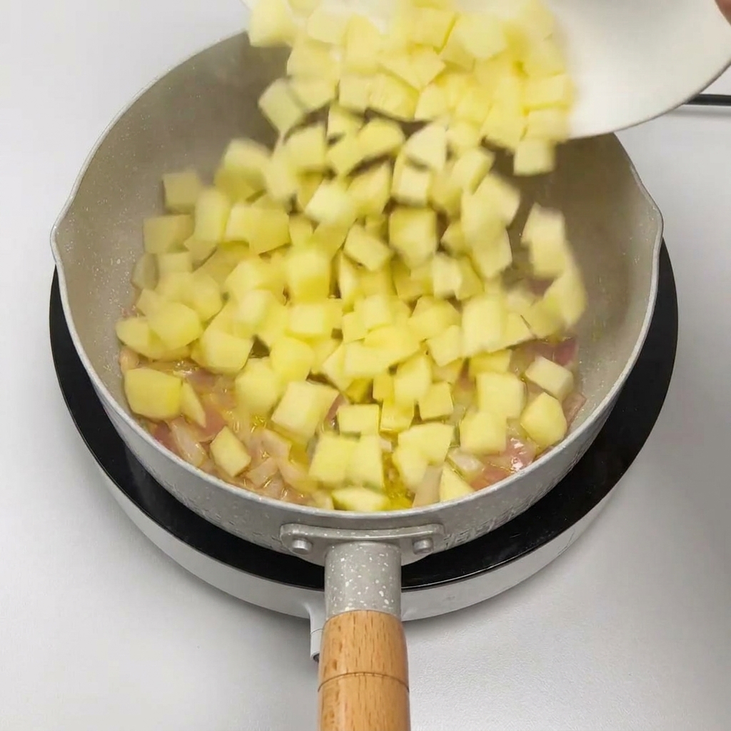 Diced potatoes sliding off a white plate into a pan with sautéed red onions.