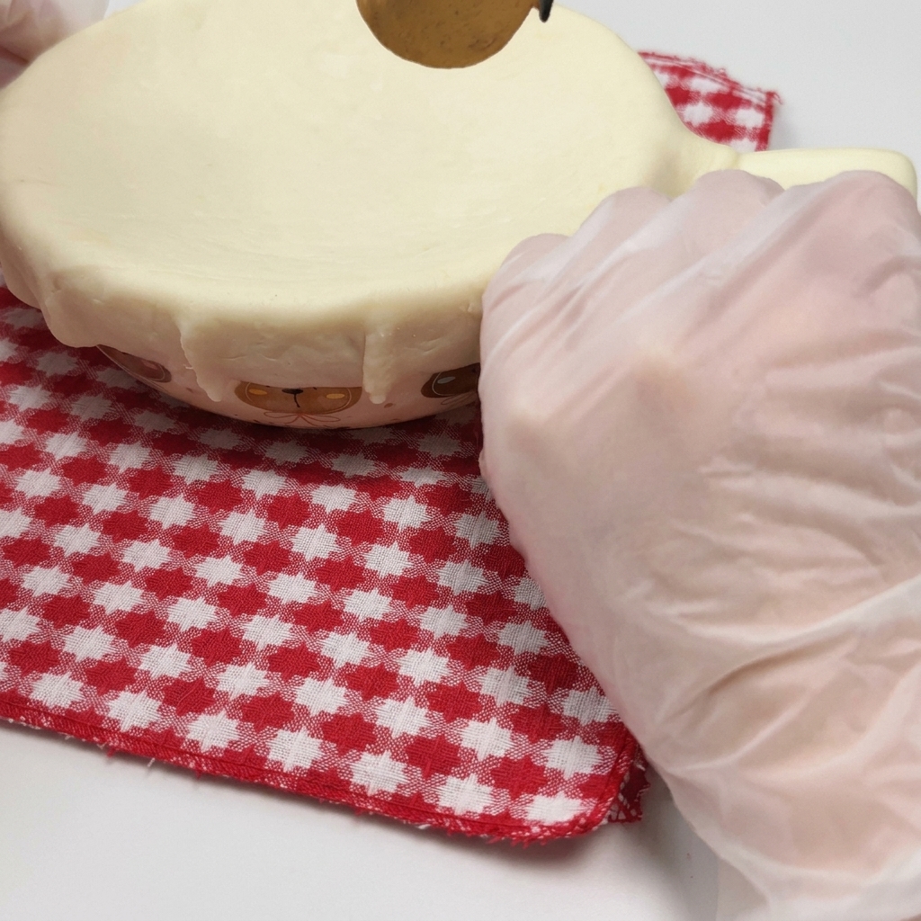 A gloved hand pressing a sheet of pastry over the rim of an oven-safe bowl to seal it.