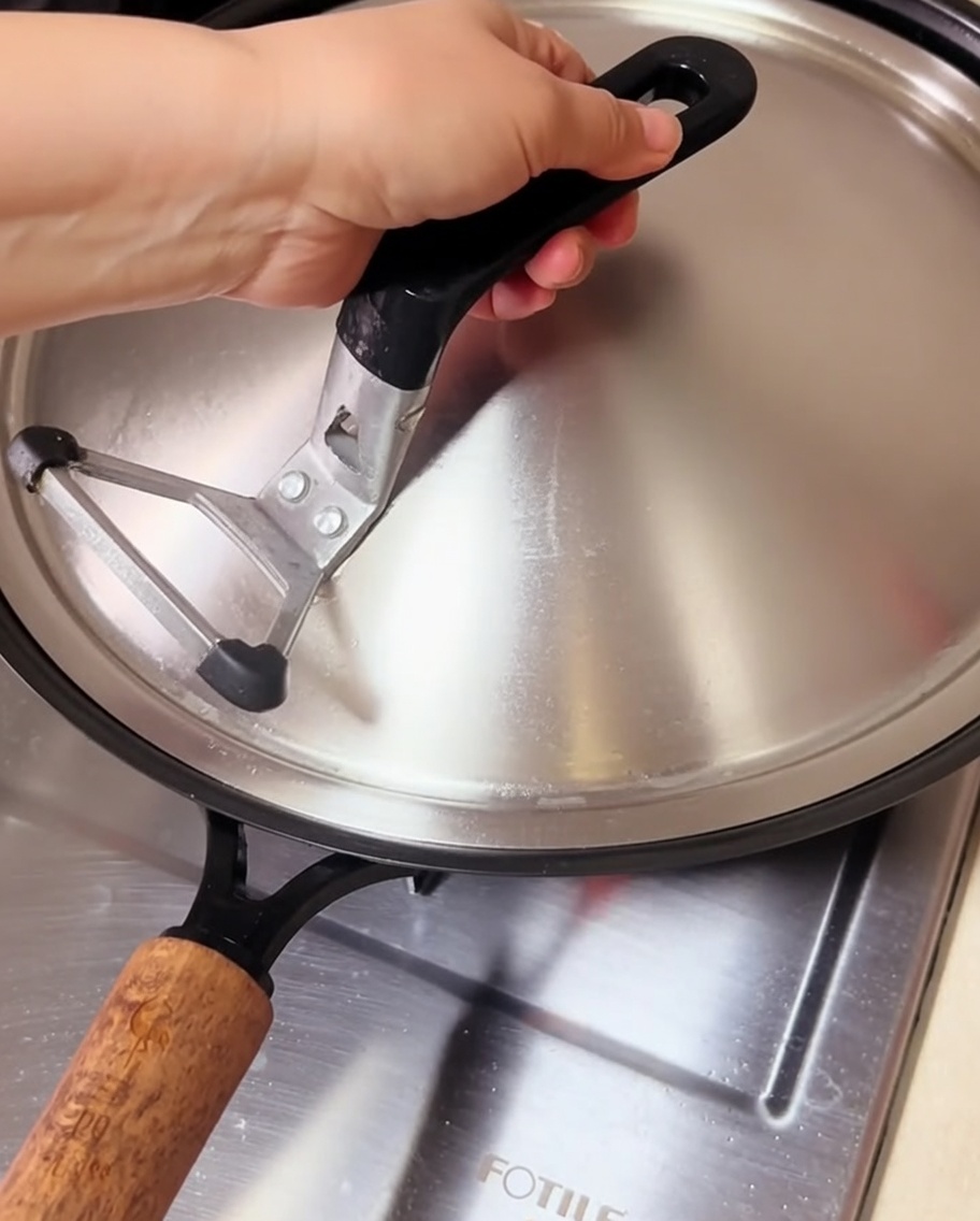 Clams cooking in a covered wok, with steam escaping from under the lid.