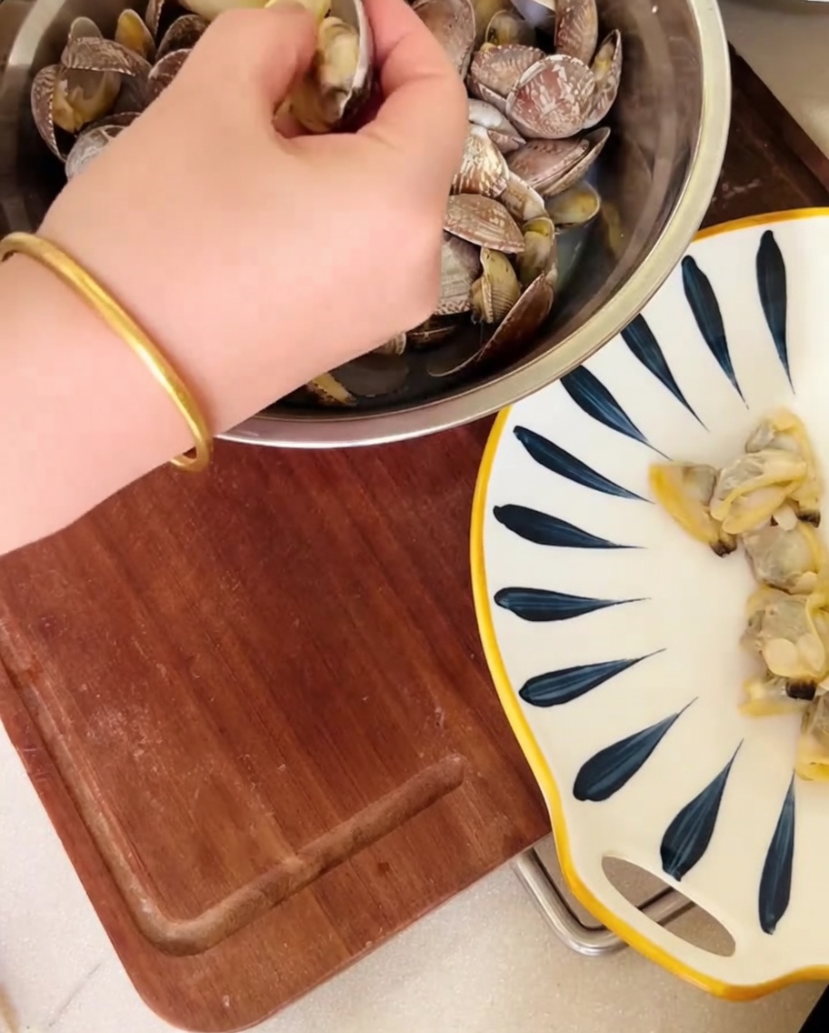 A hand removing clam meat from shells over a bowl, with the broth being reserved.