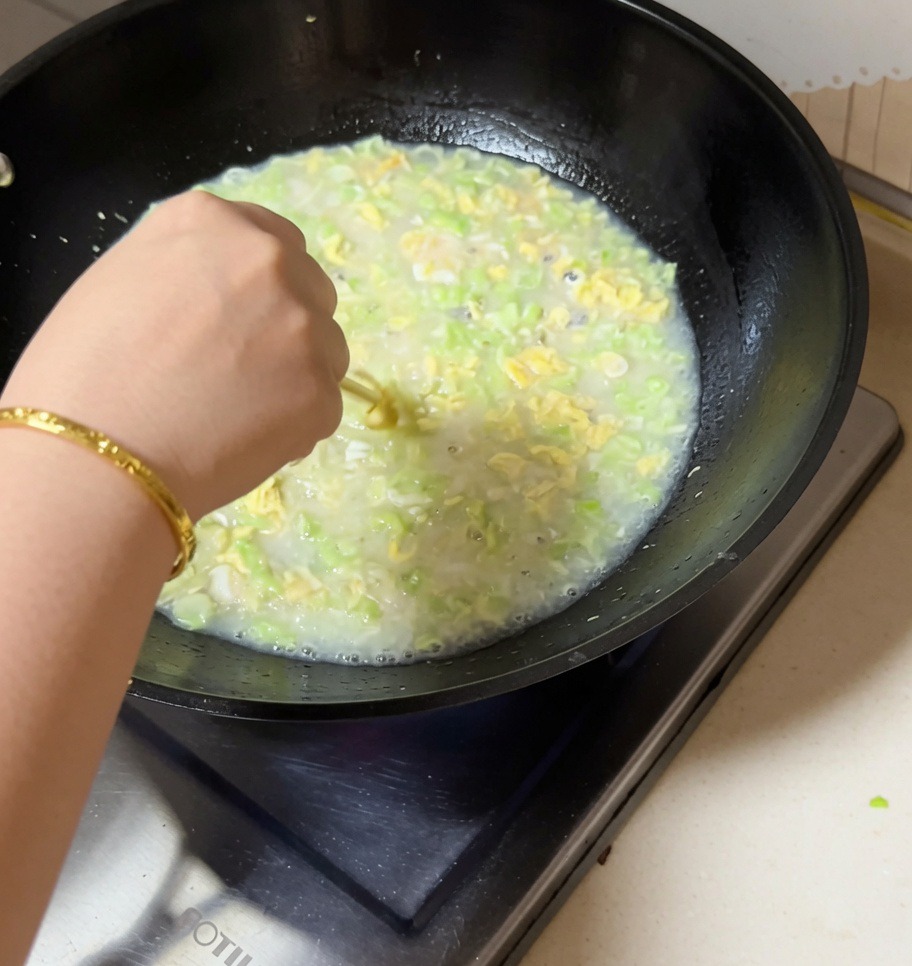 A hand stirring a bubbling wok of clam, kidney bean, and egg soup with chopsticks.