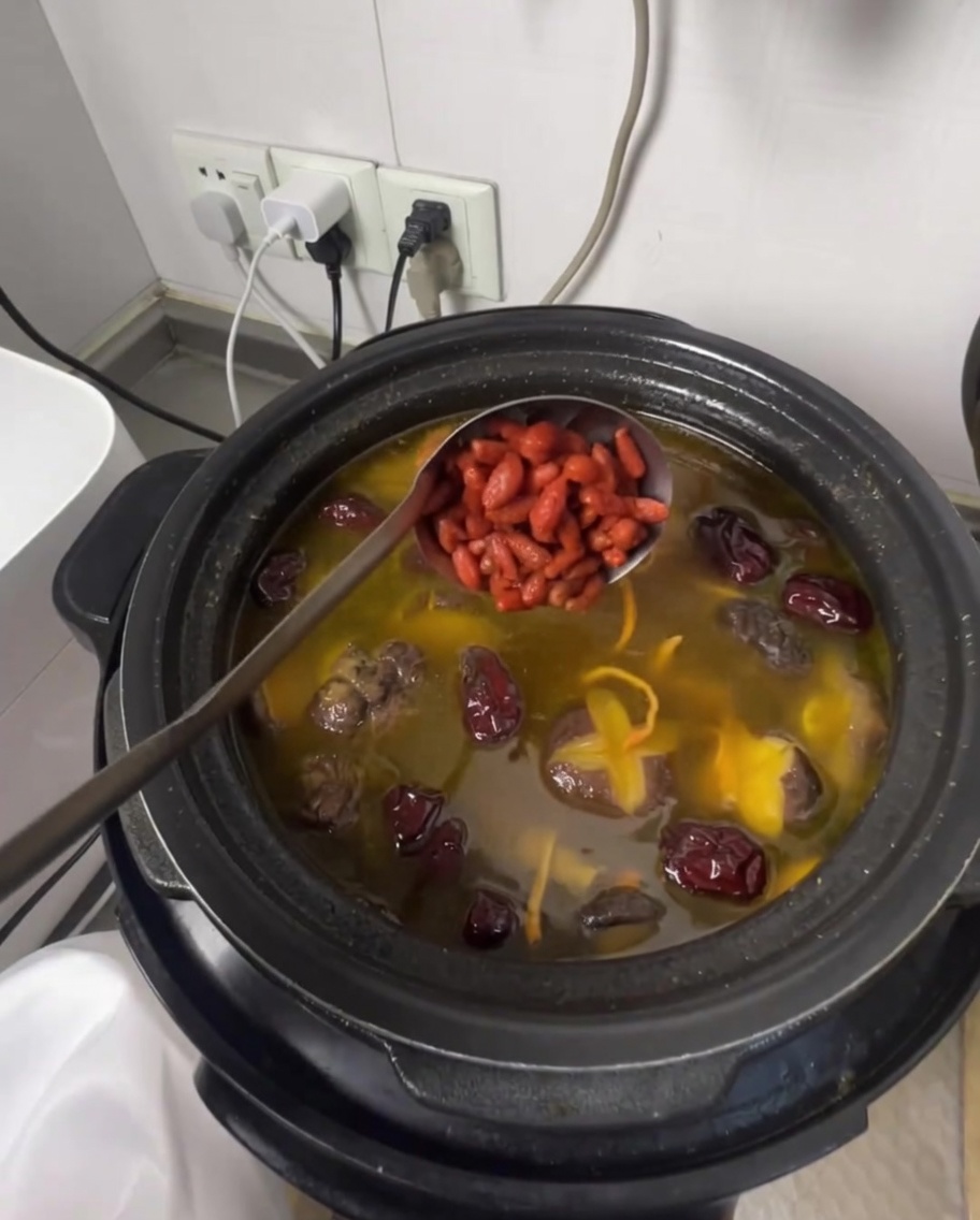 A ladle adding goji berries into the fragrant chicken soup.