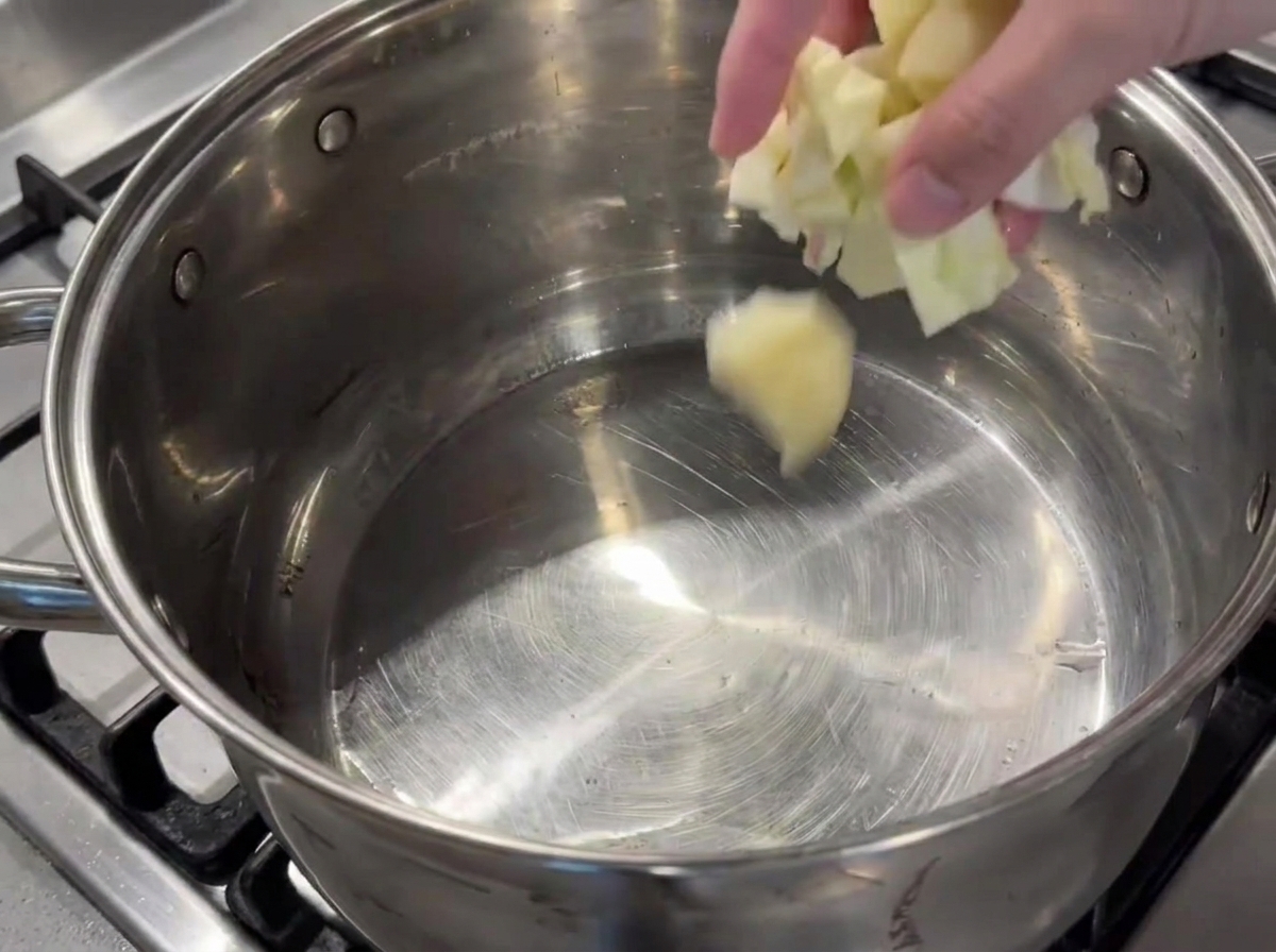 A hand adding chopped vegetables into a large oiled pot on the stove.