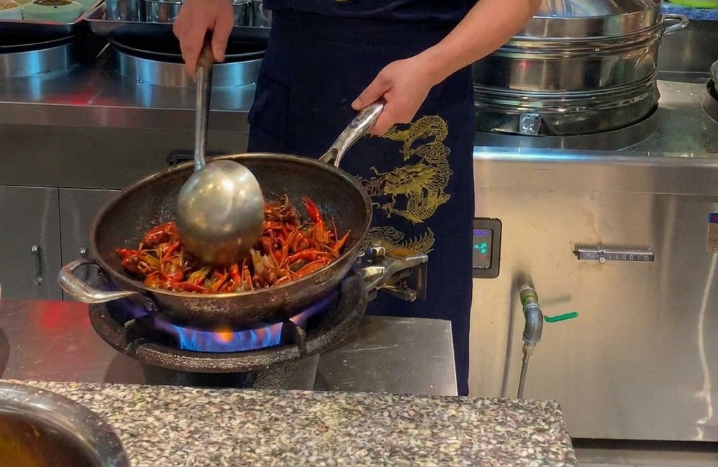 Chef stir-frying bright red crayfish in a large wok over an open flame.