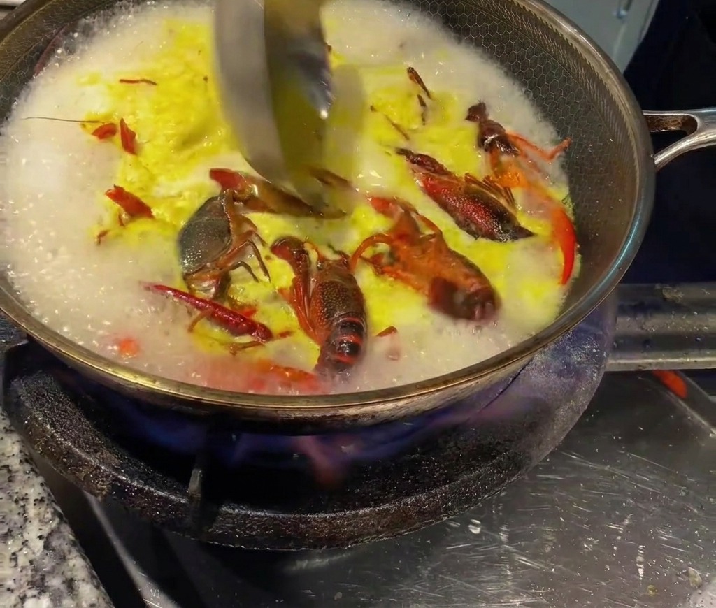 A ladle stirring concentrated chicken bouillon into the hot crayfish broth.