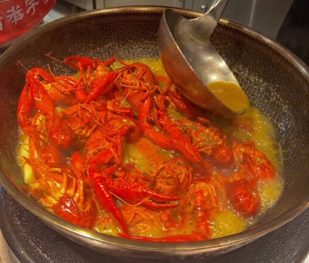 Crayfish simmering and being stirred in a reduced, thick savory broth in a wok.