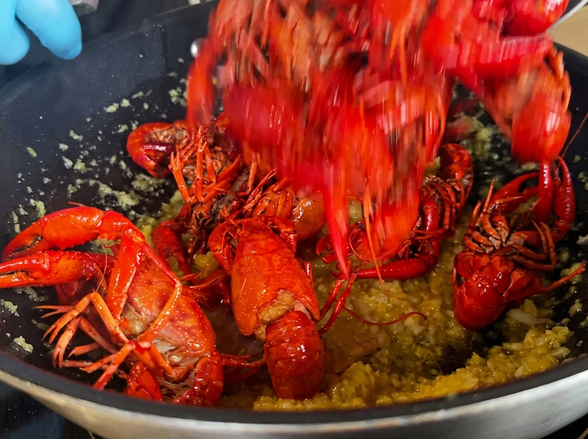 Fried crawfish being added to the wok containing the garlic base.