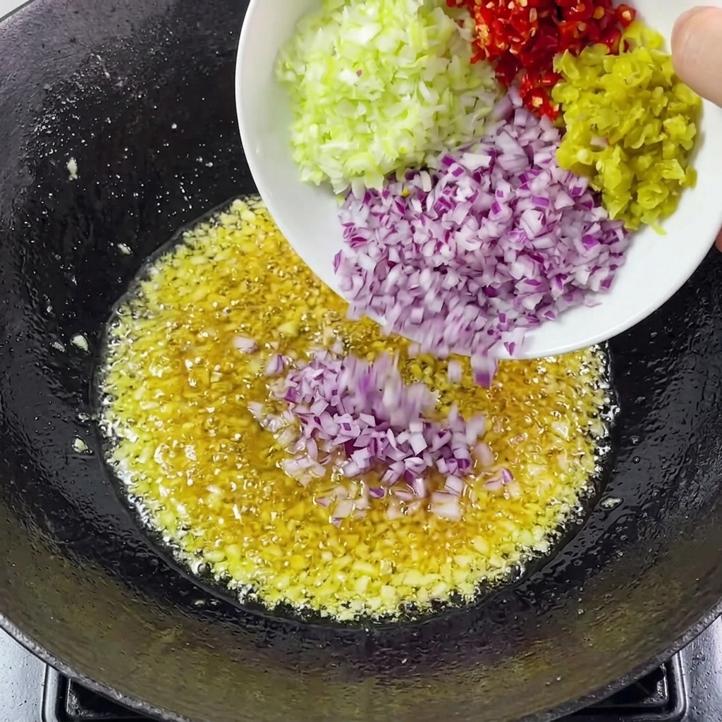 Chopped onions, scallions, and chilies being added to the garlic in the wok.