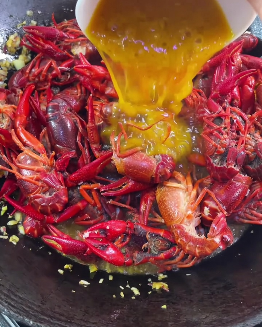 Golden pumpkin paste being poured over the crawfish in the wok.