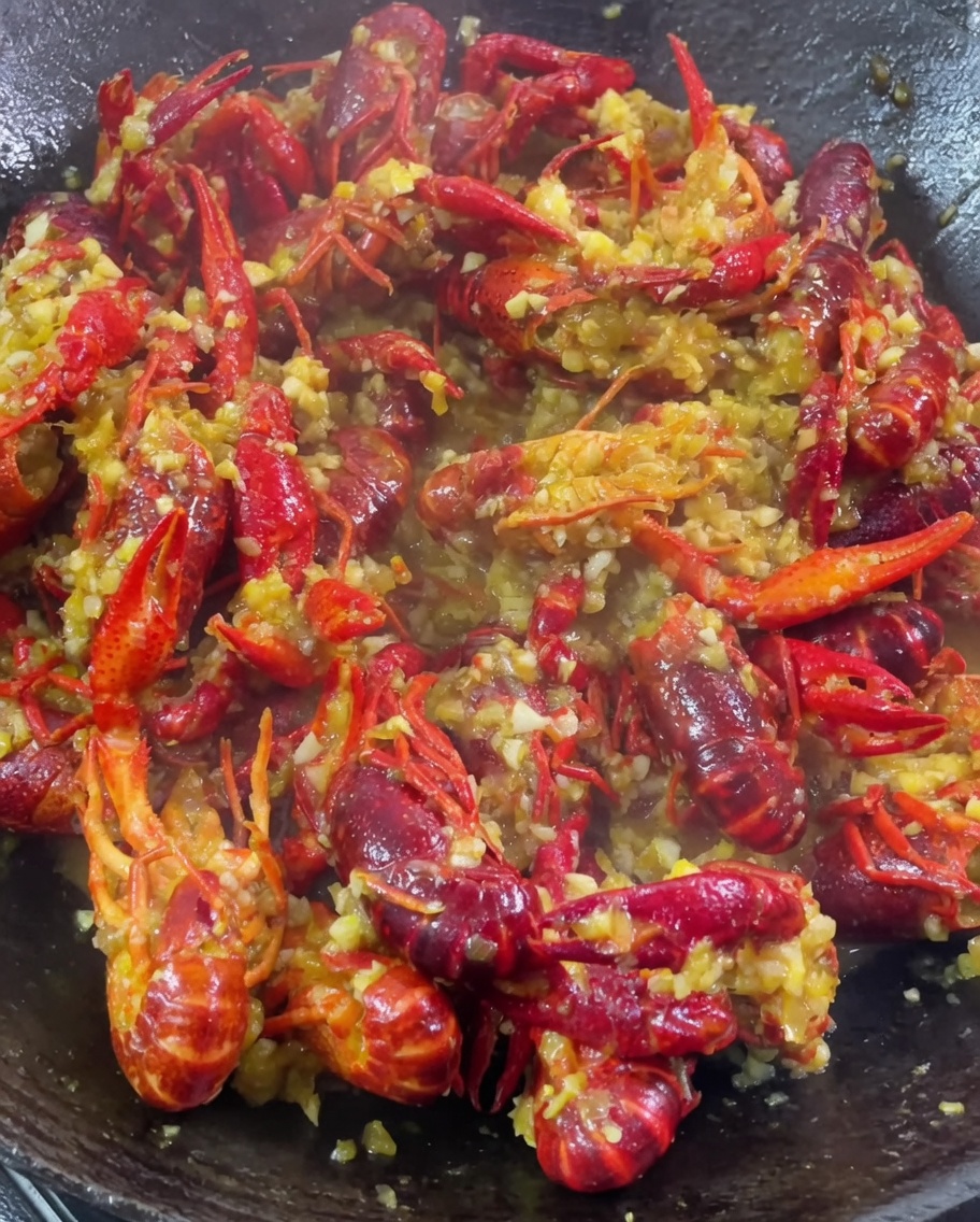 Minced garlic, curry powder, and seasonings being added to a wok of simmering crawfish.