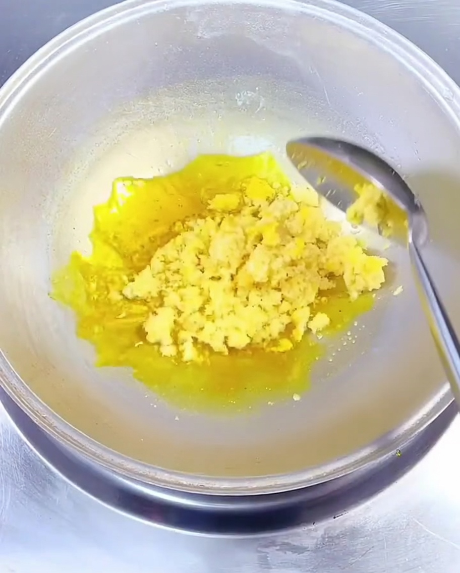 Minced garlic being stirred into hot yellow rapeseed oil in a wok with a metal spoon.