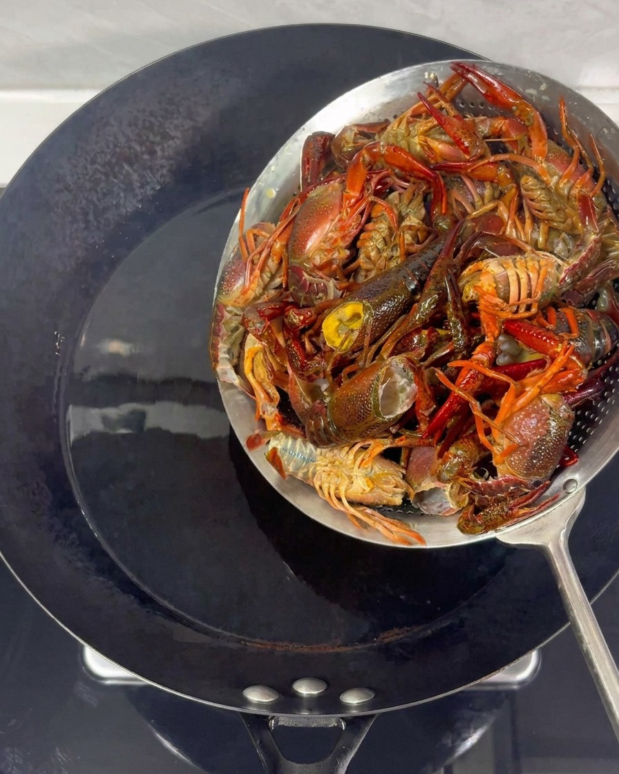 Crayfish being removed from hot oil in a wok using a metal strainer.