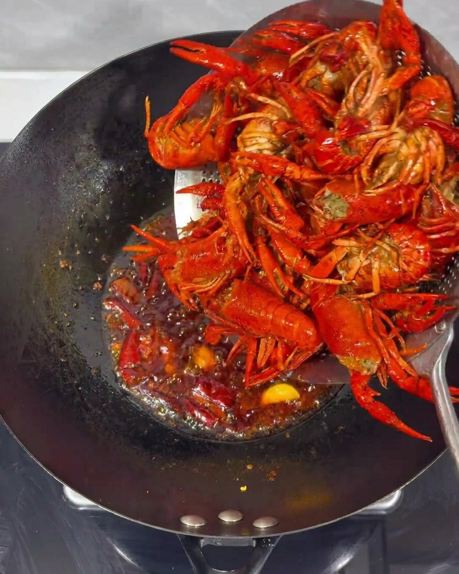 Fried crayfish being combined with the spicy sauce in a wok.