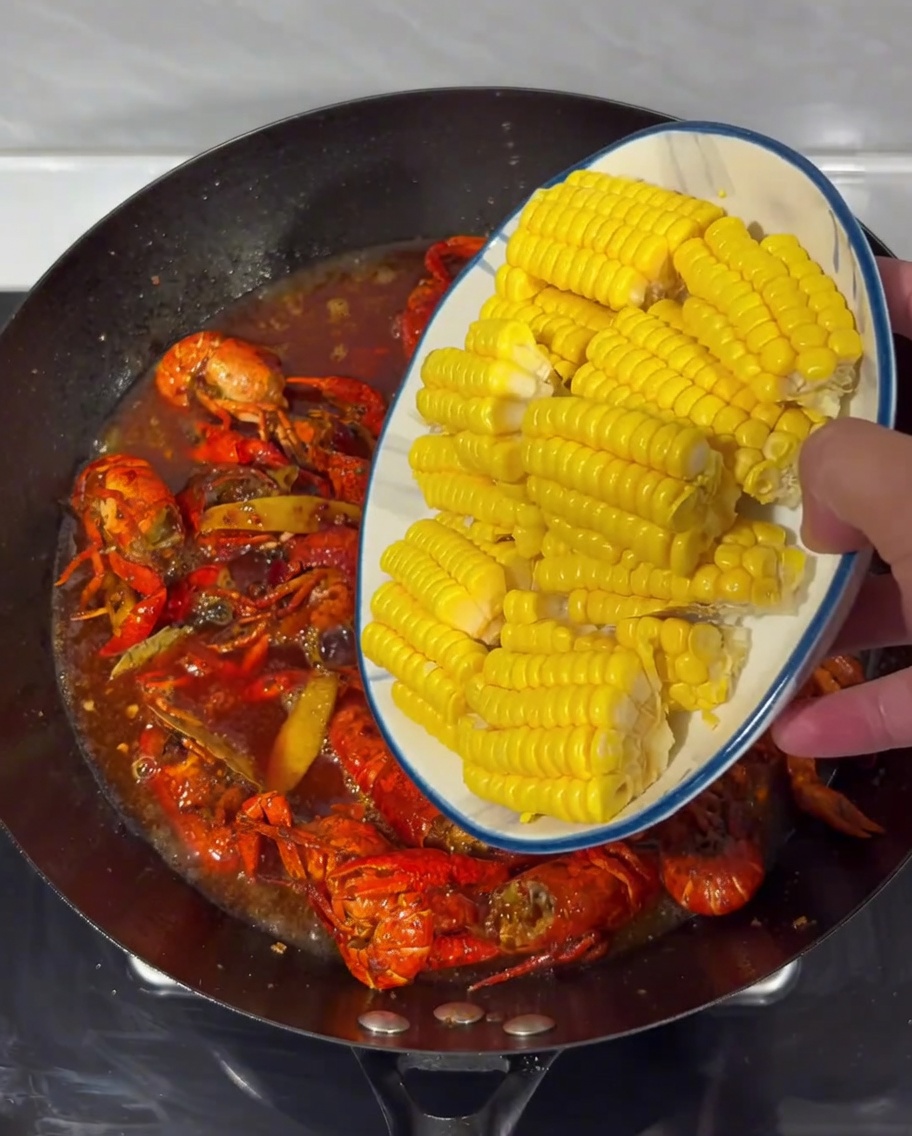 Corn pieces arranged in the spicy simmering broth with crayfish in a wok.