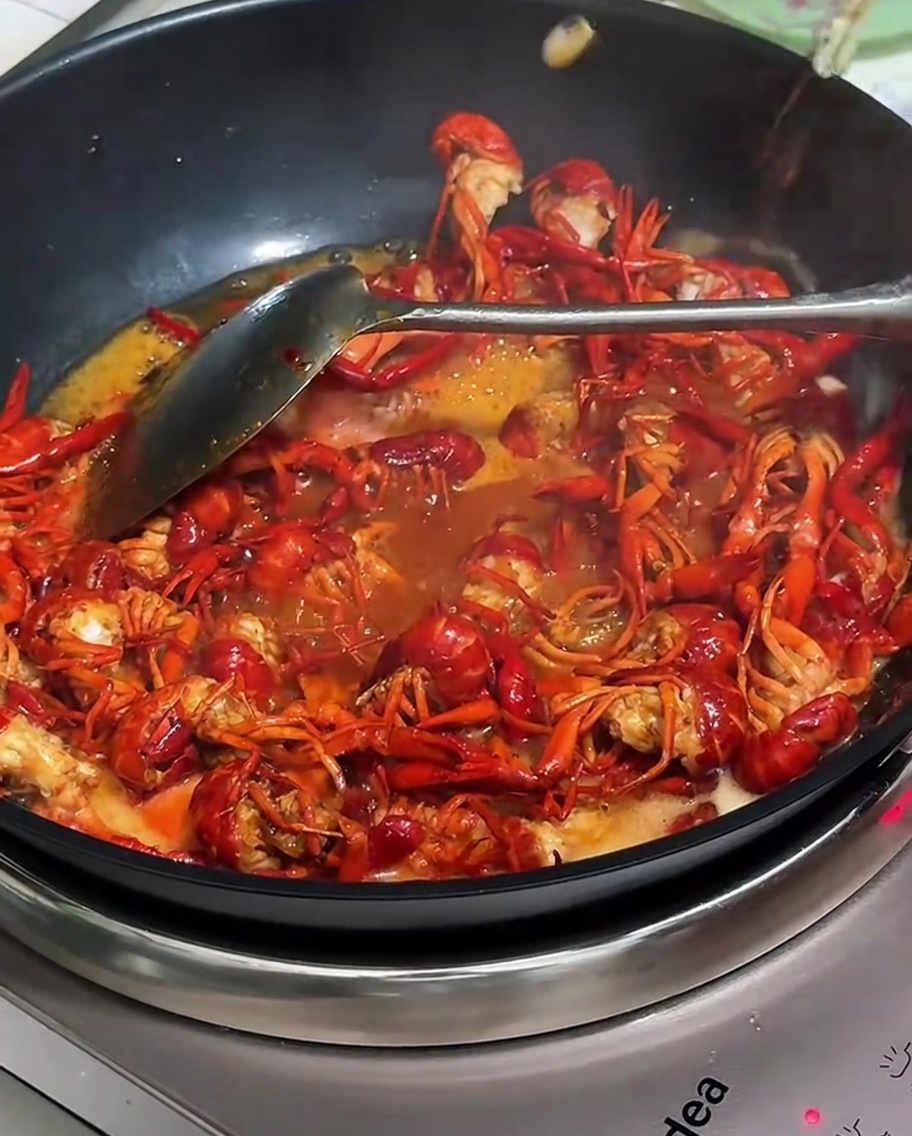 Adding the beverage and water to the simmering crayfish.