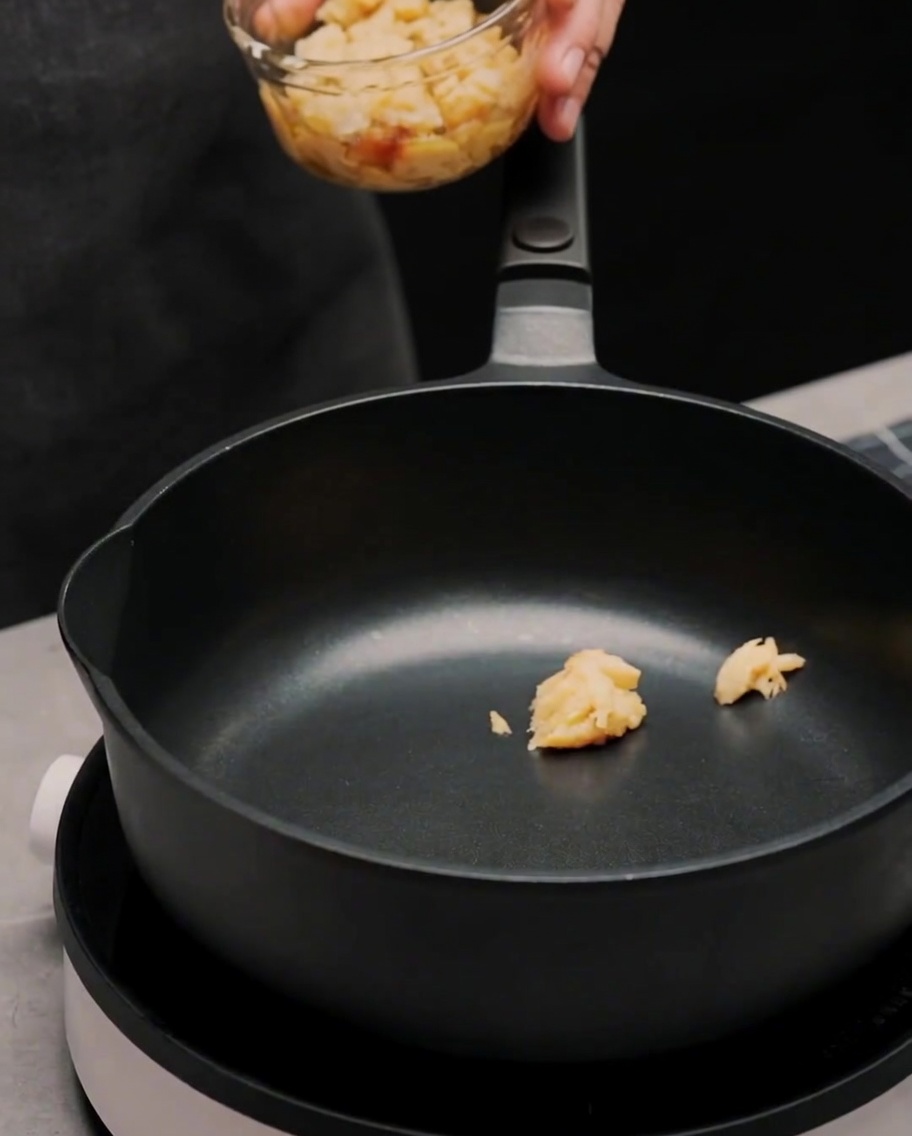 Olive oil and chili flakes being added to the pan containing garlic paste.