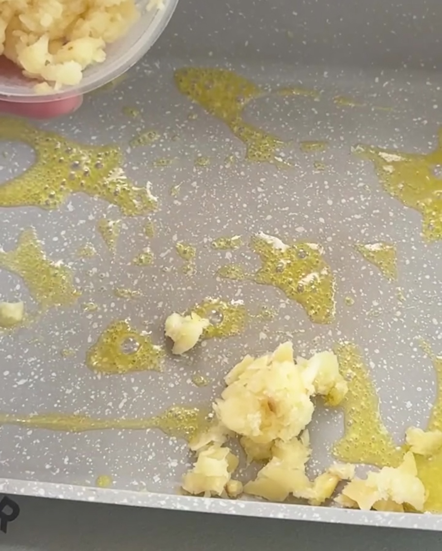 Minced garlic frying in melted butter within a rectangular pan, showing a golden brown color.