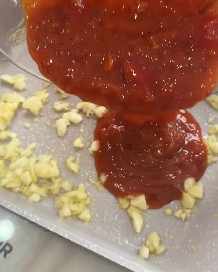 Tomato meat sauce being poured over sautéed garlic in a pan.