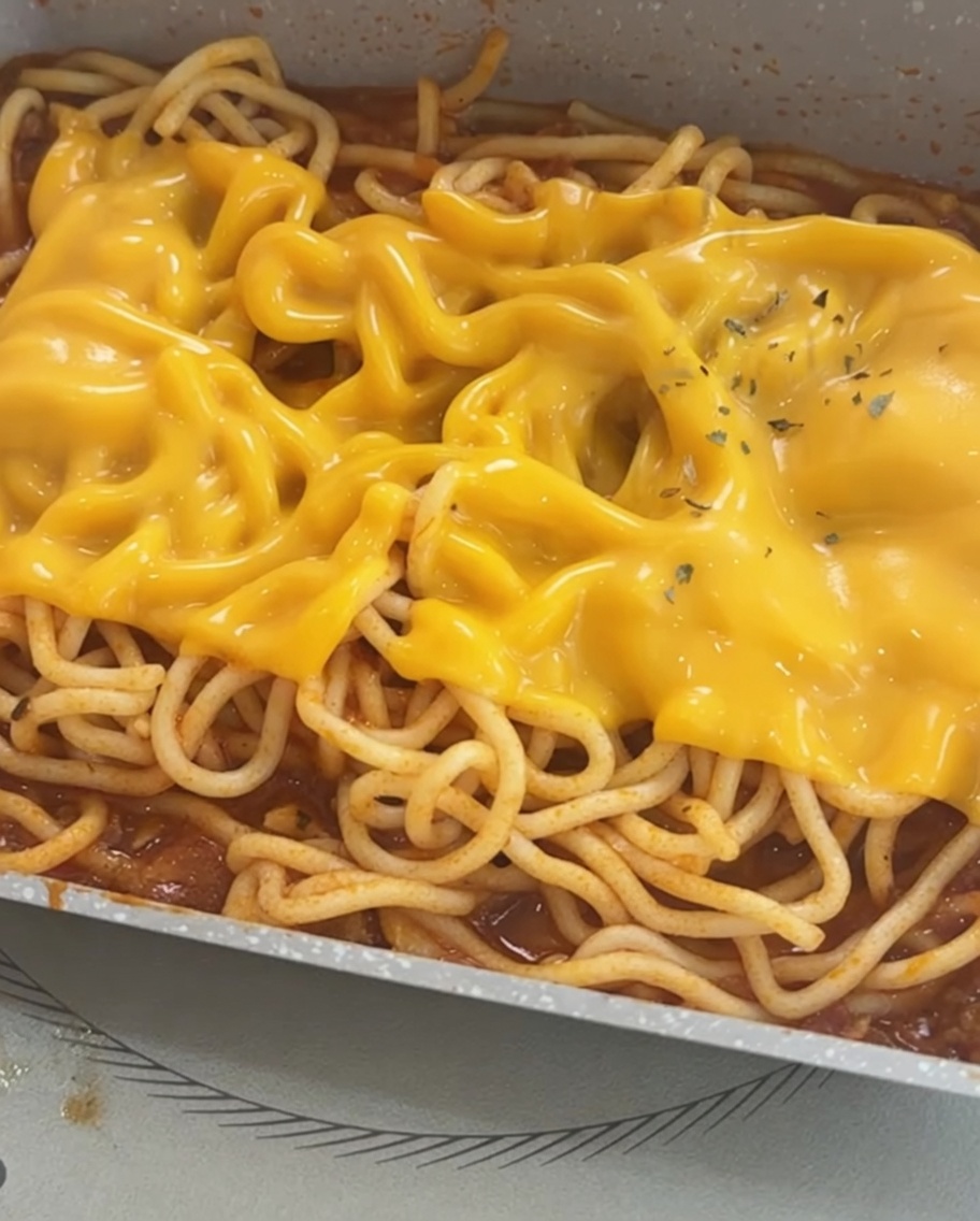 Spaghetti topped with melted cheese, finished with a garnish of dried parsley flakes.