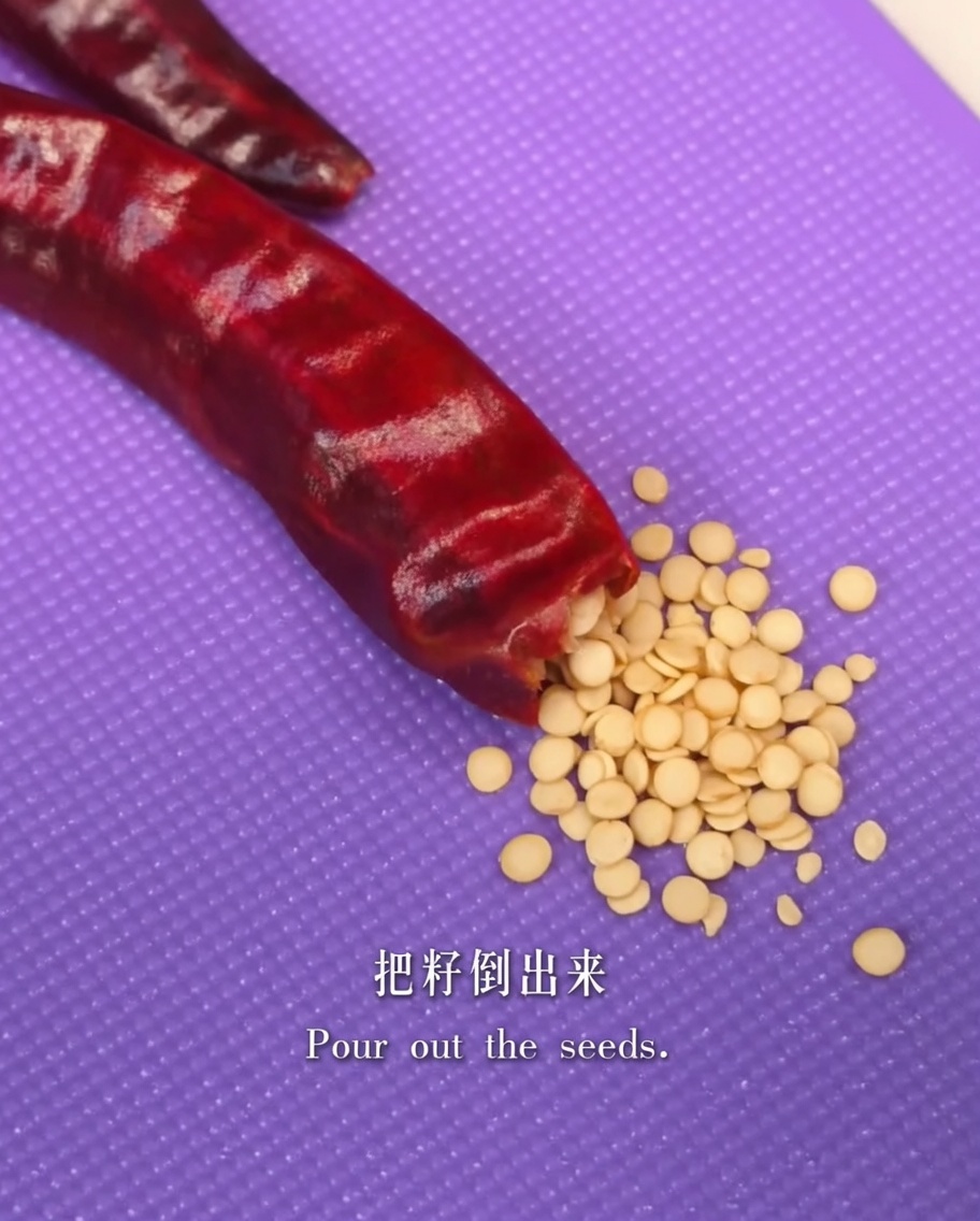 Dried red chili pepper being opened over a cutting board to remove the seeds.