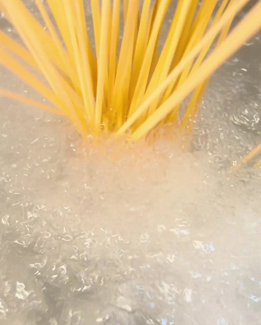 Bundle of dry spaghetti being dropped into a pot of boiling water.