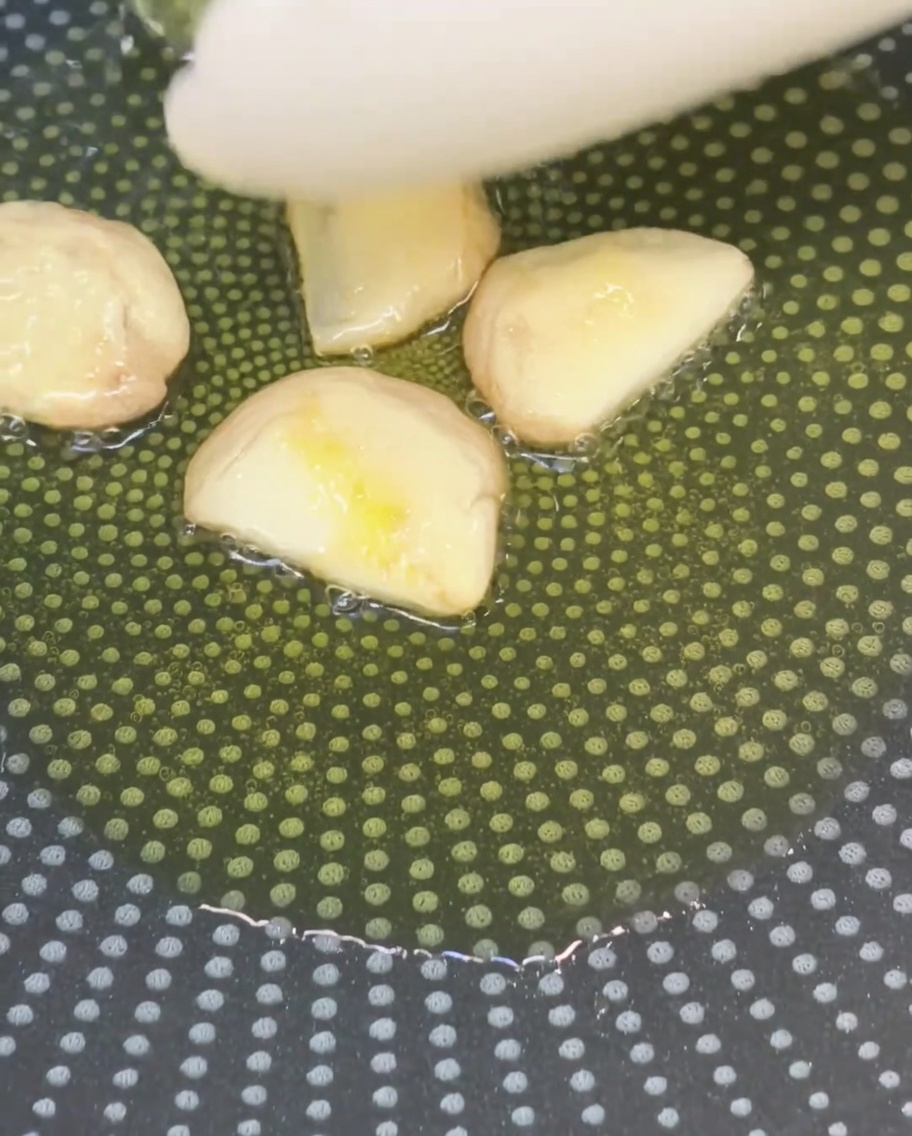 Smashed garlic cloves frying in olive oil in a non-stick pan.