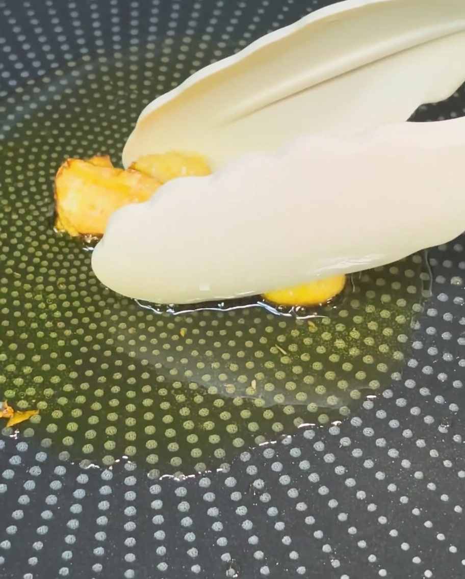 Tongs removing golden-brown fried garlic from oil in a pan.