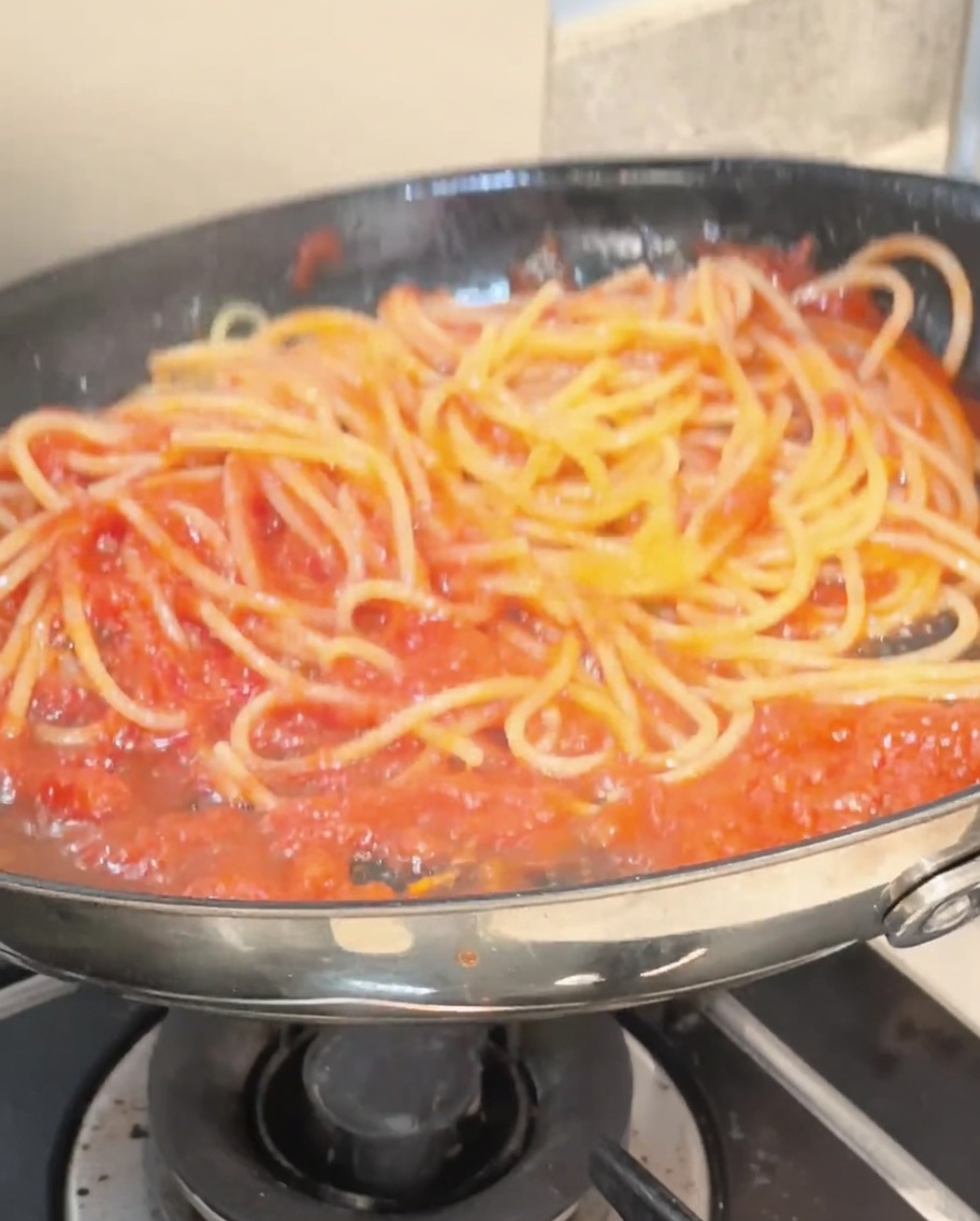 Spaghetti being tossed with tongs in a pan, fully coated in a vibrant red tomato sauce.