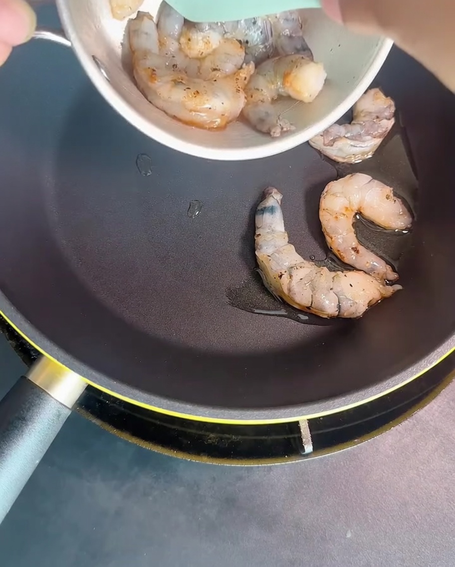 Shrimp being seared in a hot pan until they reach an opaque, cooked state.