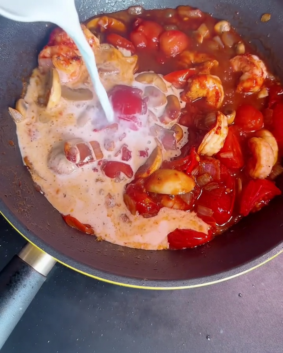Milk and starch slurry being poured into a pan with shrimp, vegetables, and sauce ingredients to thicken.