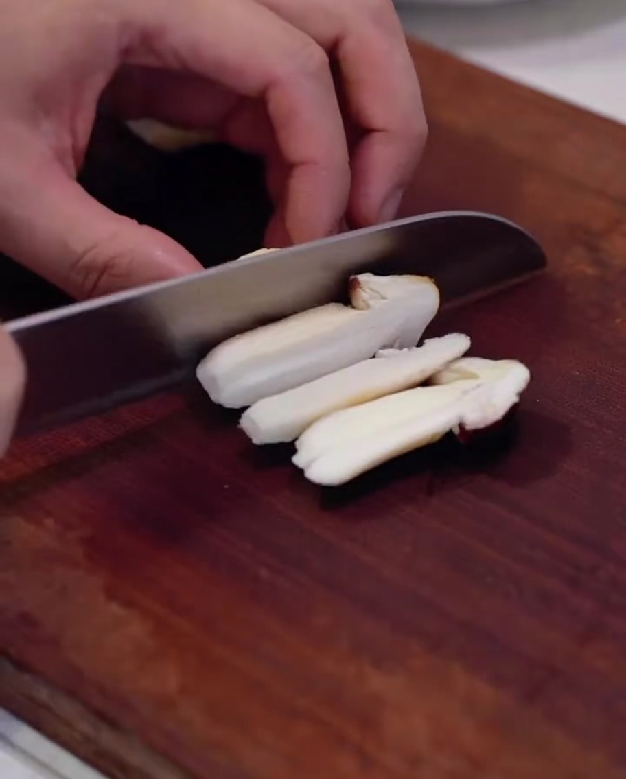 Fresh pine mushrooms being sliced on a wooden board.