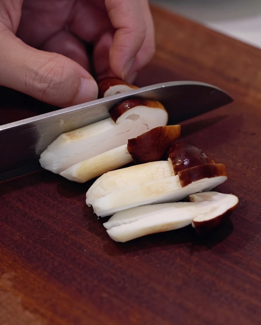 Fresh shiitake mushrooms being sliced on a wooden board.