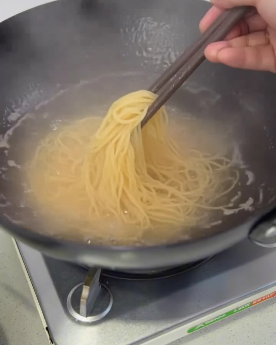 Cooked spaghetti noodles being lifted out of the pot to drain.