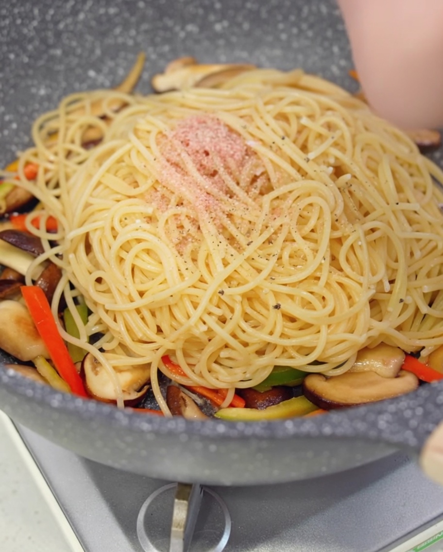 Black pepper being freshly ground over the spaghetti in the pan.