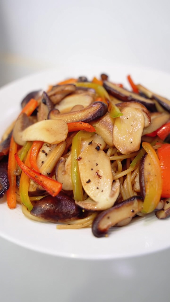 Black Pepper Mushroom Spaghetti plated with sautéed shiitake and pine mushrooms, colorful bell peppers, and fresh cracked pepper.