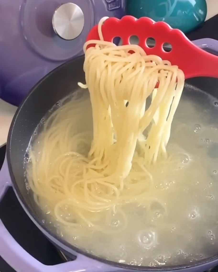 Cooked spaghetti being lifted out of the pot with a red pasta fork.