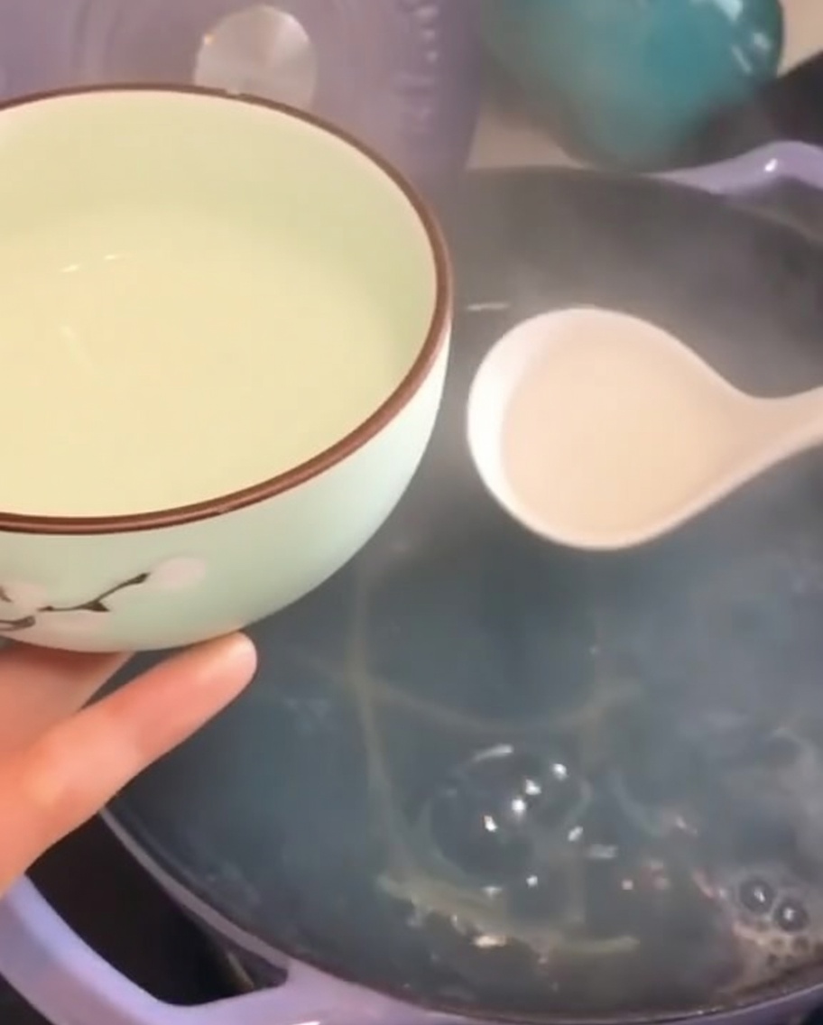 A small decorative bowl being filled with steaming, cloudy pasta cooking water using a white ladle.