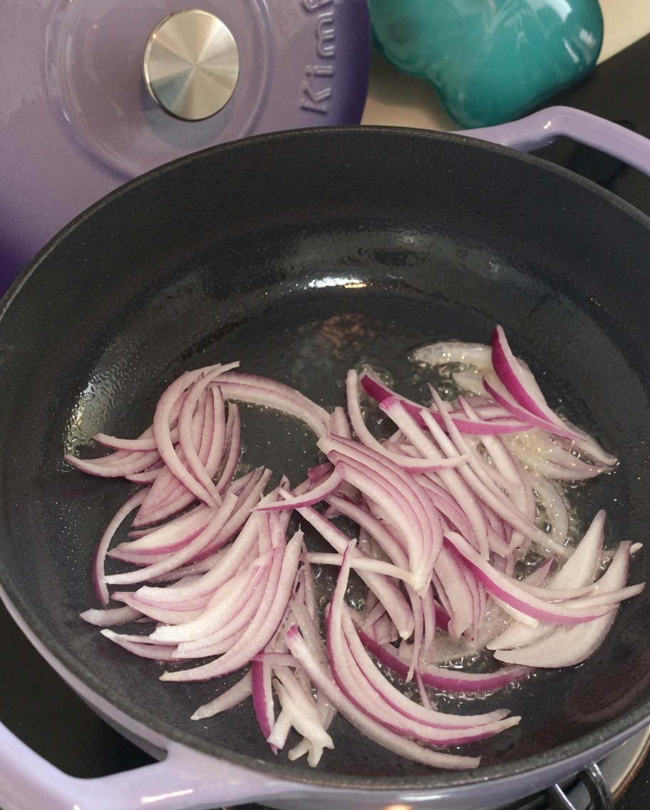 Sliced red onions sizzling in a pan with hot oil, starting to soften.